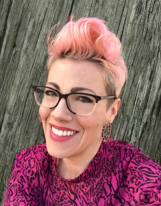 Author-illustrator Kaz Windess smiles for a portrait with pink hair and a hot pink animal print shirt.