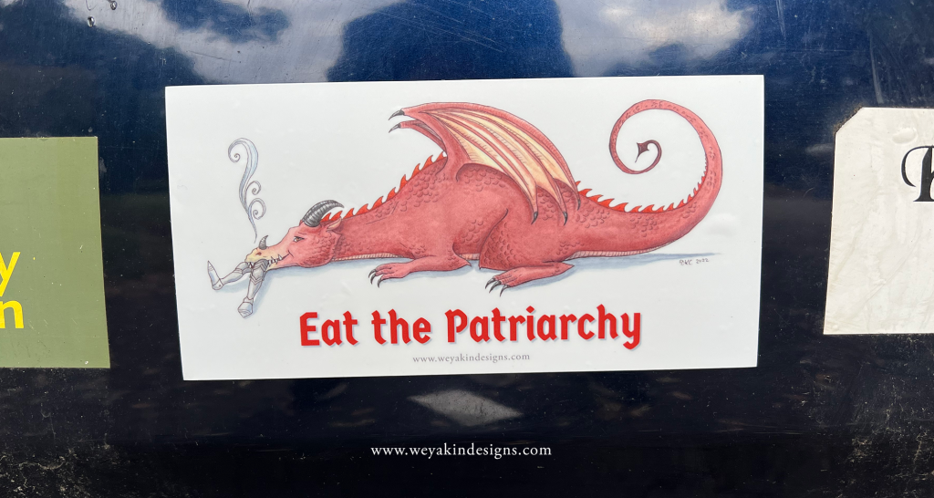 A dragon bumper sticker on a navy blue car next to other bumper stickers.