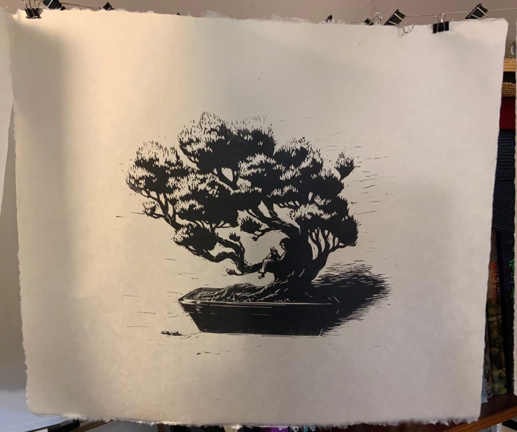 A print of a bonsai tree with somebody reading a book while lying on a branch. The print is hung by clips on a line to dry after printing. Art by Sarah LuAnn Perkins.