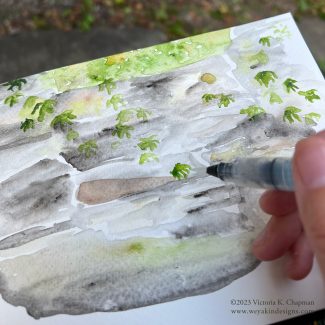 A hand of someone painting green leaves in a watercolor journal. www.weyakindesigns.com