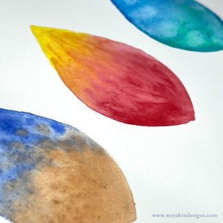 Three teardrop shapes in a row painted with different colors and textures in watercolors.