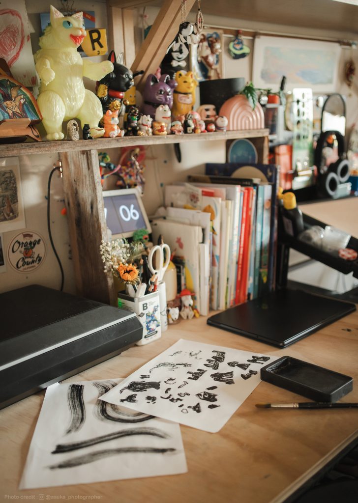 Part of Shiho's desk with sumi ink drawings, books, and toys.