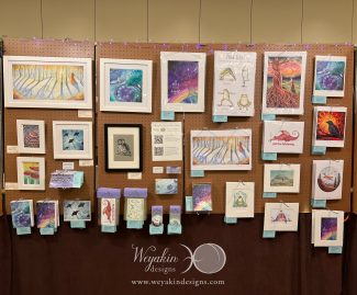 A display of Victoria's art on a brown peg board panel at Arisia in January of 2024. 